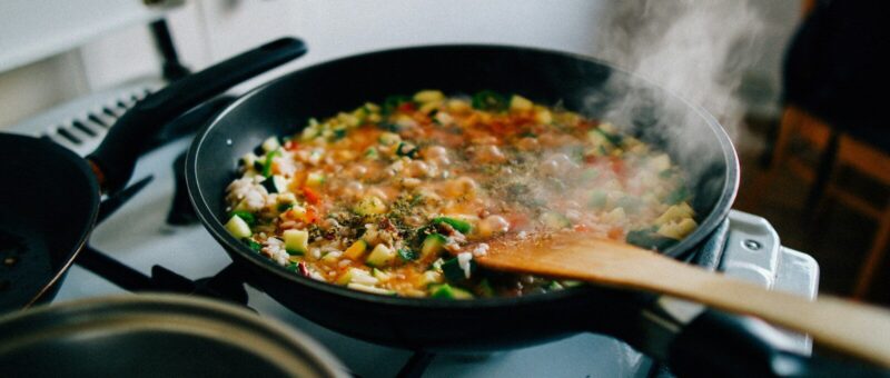 A pan of food cooking on a stove with a wooden spoon